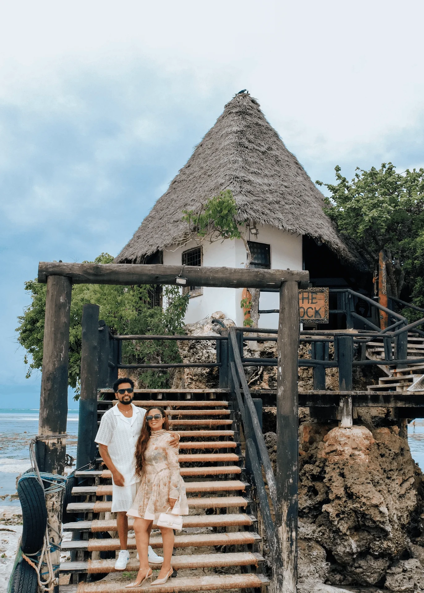 Standing on the steps below the thatched roof, couple photoshoot in Zanzibar